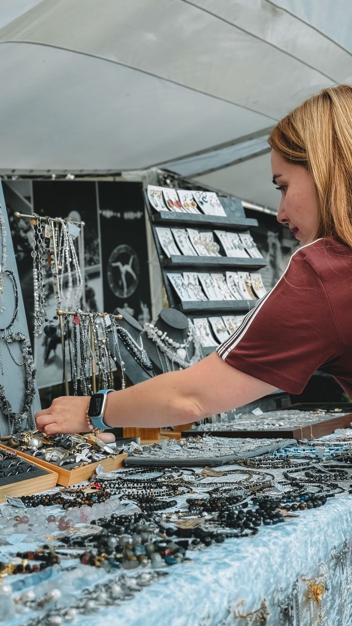 Young woman browsing bracelets and necklaces at an outdoor market stall.
