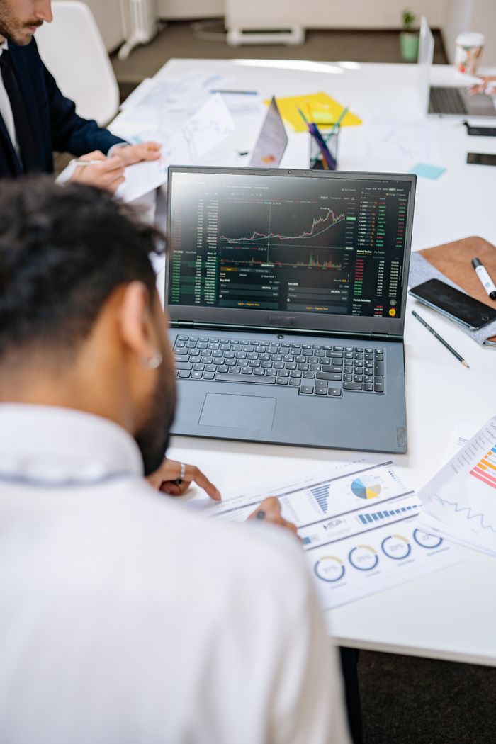 get-in-touch Business professionals analyzing stock charts and graphs on a laptop in an office setting.